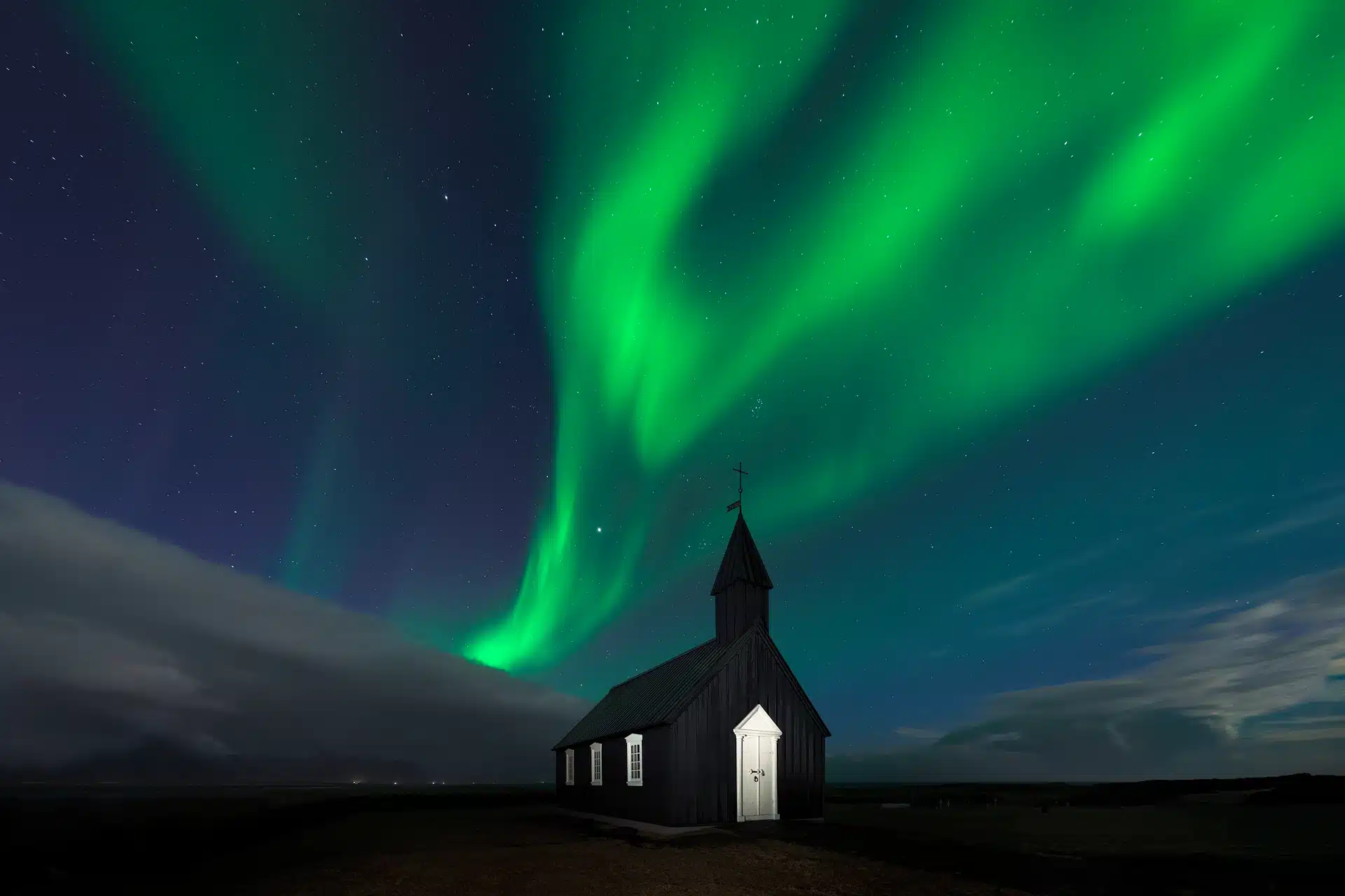 Northern Lights over a small black wooden church in Iceland at night.