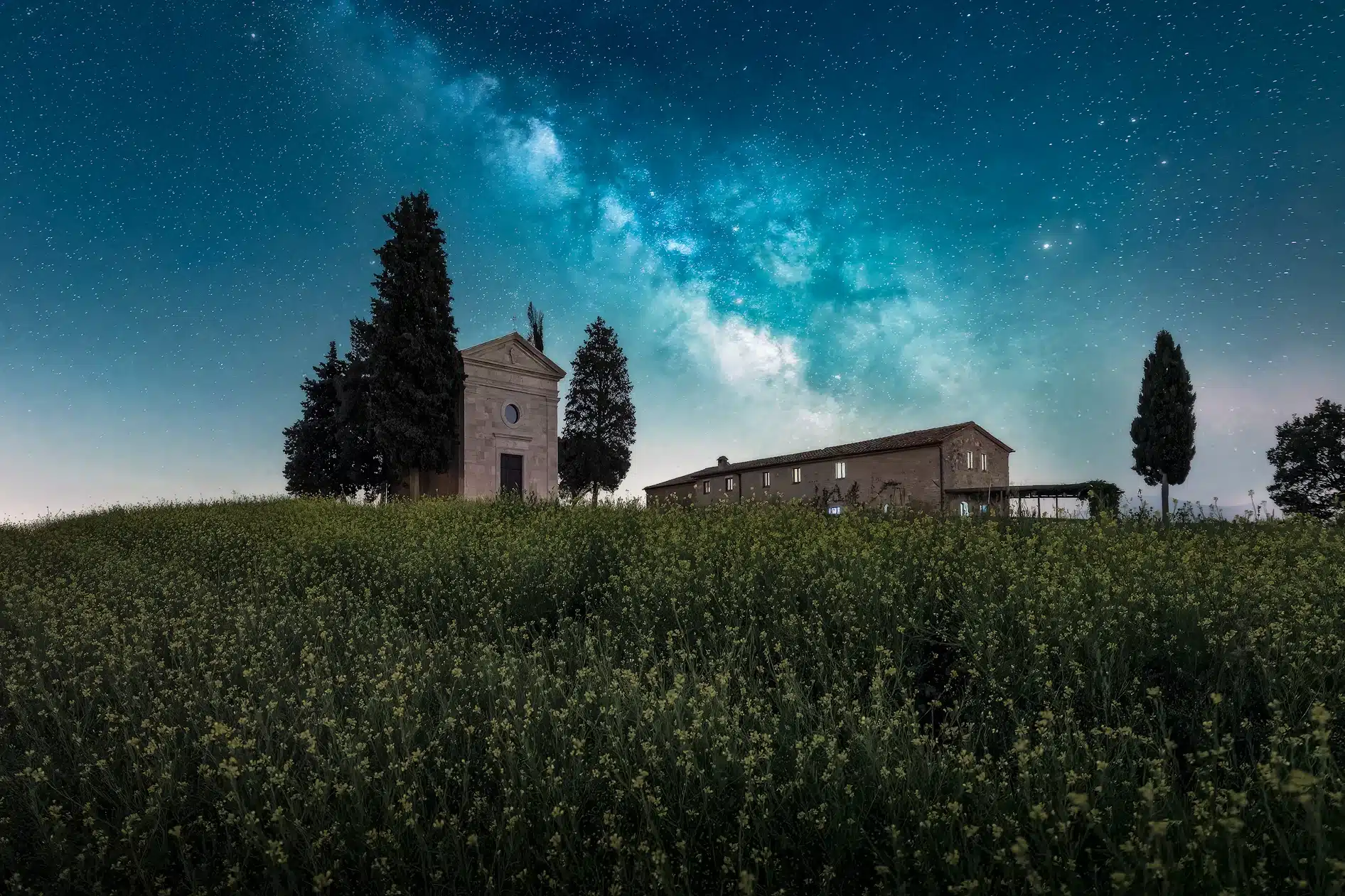 Small Tuscan chapel and farmhouse beneath a starry night sky with the Milky Way.